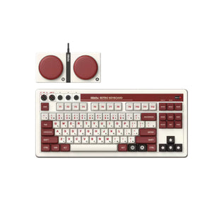 A person using the 8BitDo Retro 108 mechanical keyboard with a retro-style dual-button controller, tapping red action buttons labeled A and B. The keyboard features vintage white and maroon keycaps, placed on a wooden desk beside a colorful game screen — perfect for nostalgic gaming and creative typing.