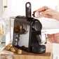 A hand loading a coffee capsule into the De'Longhi Essenza Mini EN85WAE capsule coffee machine, with pastries in the background.