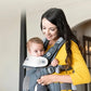 Mother carrying baby in Joie Savvy Air 4-in-1 Baby Carrier in front-facing position. The carrier supports natural bonding, includes padded headrest, and features breathable AirMesh fabric for all-day comfort.
