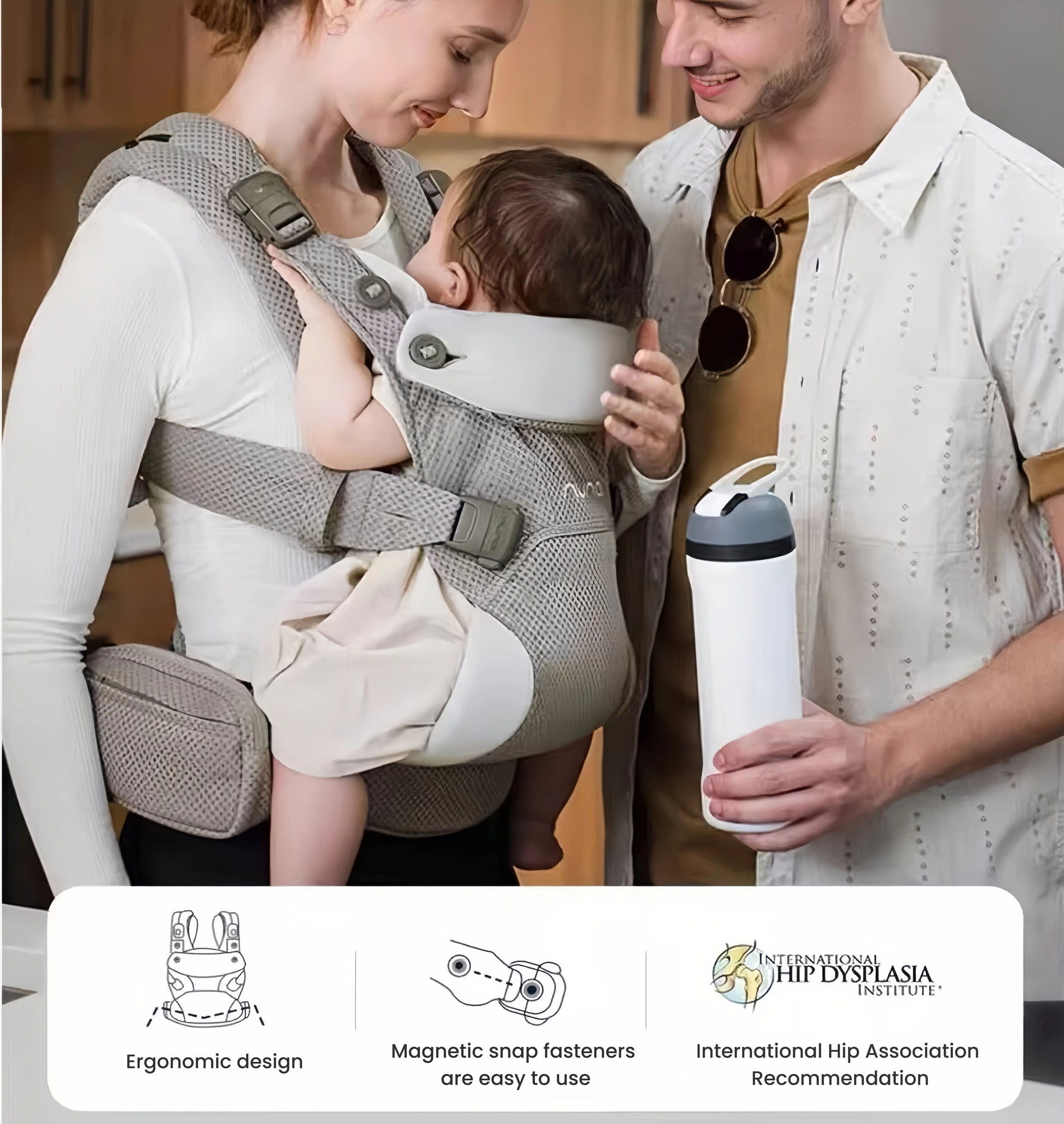 Mother wearing Nuna Cudl Clik Carrier with newborn in front-facing-in position. Features highlighted: ergonomic design, magnetic snap fasteners, and International Hip Dysplasia Institute recommendation. Partner standing beside her holding water bottle.