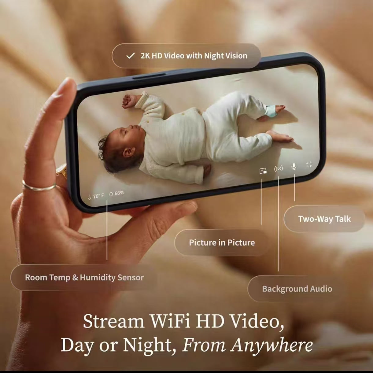 Hand holding smartphone displaying Owlet Dream Sight baby monitor app with 2K HD video, night vision, two-way talk, picture-in-picture mode, background audio, and room temp & humidity sensor