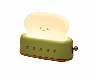 Green toaster-shaped night light with smiling toast slice glowing warm white and TOAST text on base, side angle on white background