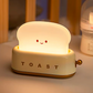 White toaster night light glowing on nursery dresser beside baby feeding bottle showing gentle bedside lamp glow