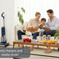 The Tineco FLOOR ONE S5 PLUS is shown in its charging dock in a living room, illustrating how it easily charges and stores neatly while a happy family relaxes in the background.